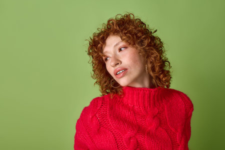 A young woman with red curly hair in a red sweater, surrounded by green.