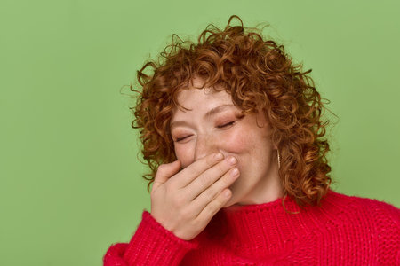 A young woman with red curls laughs joyfully against a green background.