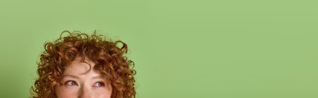 Young woman with curly red hair smiles in a cozy red sweater against a green wall, banner