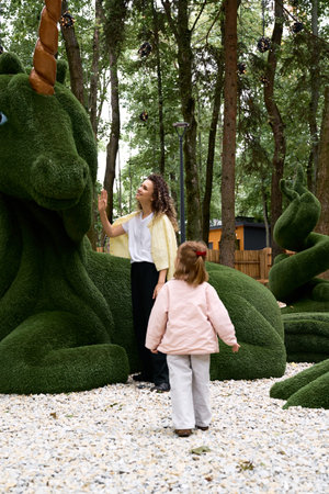 A young mother and her daughter explore a vibrant amusement park with enchanting sculptures.の写真素材