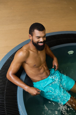 A shirtless man with a beard sits peacefully in a spa center, embracing relaxation.