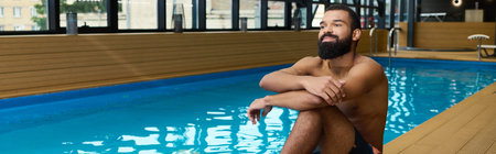 A shirtless African American man with a beard enjoys a peaceful moment by the pool in a spa, banner