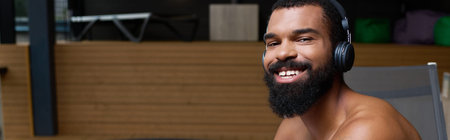 A shirtless Black man with a beard and headphones relaxes at a tranquil spa center, banner