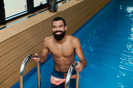 Shirtless African American man enjoys a peaceful moment in a wellness spa area.