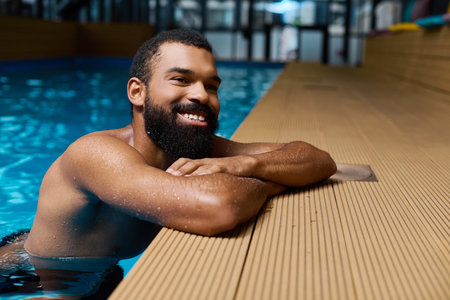 A happy man leans comfortably against the side of a tranquil pool, soaking in wellness.