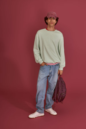 Confident young man dressed in casual yet fashionable attire stands against a rich background.
