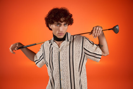 A young handsome man showcases his fashion sense while holding a golf club, exuding charm.