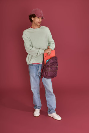Handsome man displays contemporary style with a backpack while posing in a colorful venue.