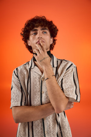 Handsome man in a fashionable shirt poses thoughtfully against a striking orange background.