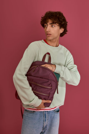 Handsome man showcases his fashion sense while holding a stylish backpack in bold colors.