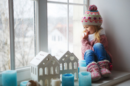 little girl on a window sill looks at the streetの写真素材