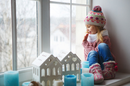 Little girl sitting on a window sill and looks at the streetの写真素材