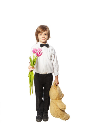 Boy with flowers and a teddy bear standing on a white background in a shirtの写真素材