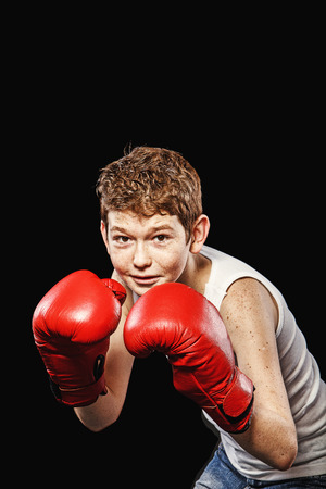 Red-haired boy on a black background with red boxing glovesの写真素材