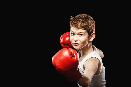 Red-haired boy on a black background with red boxing glovesの写真素材