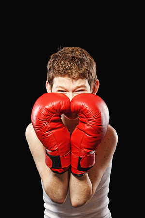 Red-haired boy on a black background with red boxing glovesの写真素材