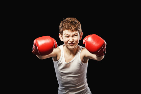 Red-haired boy on a black background with red boxing glovesの写真素材