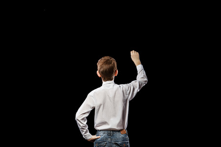 Red-haired boy standing with his back against a black background and something draws