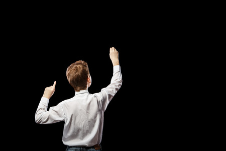 Red-haired boy standing with his back against a black background and something drawsの写真素材