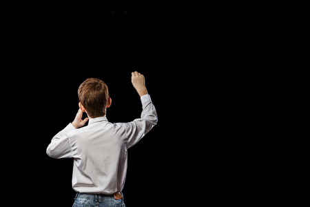 Red-haired boy standing with his back against a black background and something drawsの写真素材