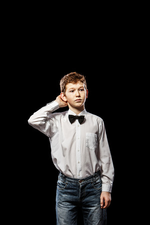 The red-haired boy on a black background with a white shirt thinkingの写真素材