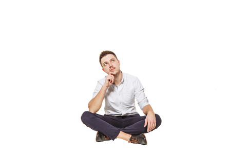Young and handsome guy in shirt and trousers sitting on a white backgroundの写真素材