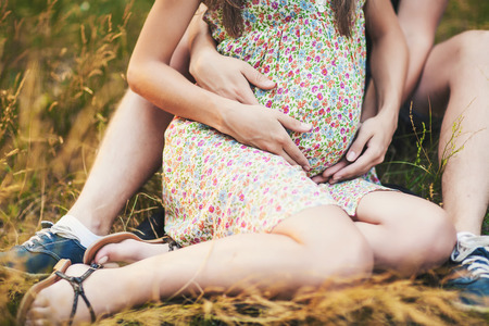Pregnant girl in sundress on the grass with her husbandの写真素材