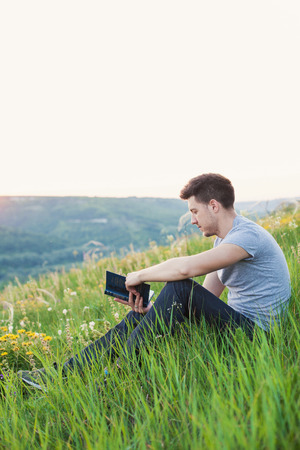 man sitting on the hill and reading a book on background nature verticalの写真素材