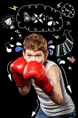 Red-haired boy on a black background with red boxing glovesの写真素材