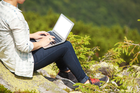 Woman with laptop sitting on a stone in the mountainの写真素材