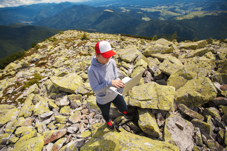 Woman with laptop standing on a stone in the mountainの写真素材