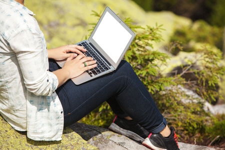 Woman with laptop sitting on a stone in the mountainの写真素材