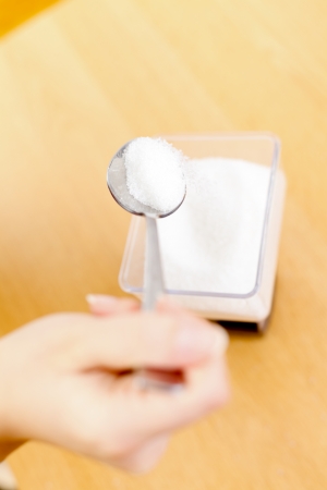 Woman pouring sugar into a kitchen scale with spoon.の写真素材