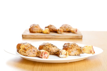 Three raw pickled chicken legs on a white plate on the table and in the background another three chicken leg on a wooden plate.の写真素材
