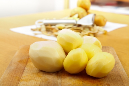 Peeled potatoes on wooden plate on the table, in the background a peeler and potatoes - horizontal.の写真素材