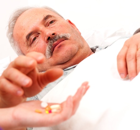 Elderly man laying in bed taking pills - focus on eyes.の写真素材