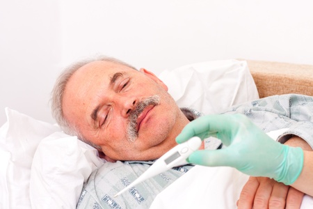 Elderly man laying in bed, nurse taking temperature.の写真素材