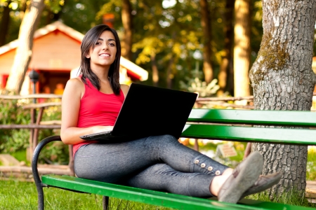 A beautiful young woman laying on bench and working on laptop outdoors.の写真素材