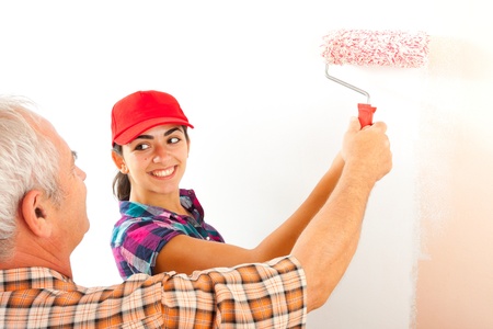 Senior man teaching his daughter how to use the paint roller.の写真素材