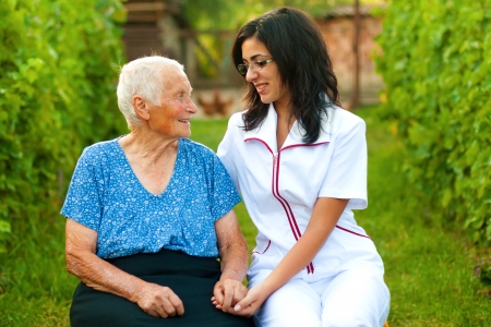 A young doctor / nurse chatting with an elderly sick woman holding her hands with caring attitude.の写真素材