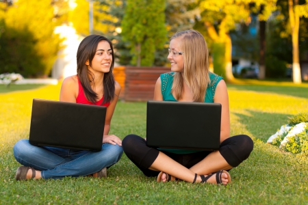 Girlfriends sitting and chattings outdoors with laptops on their lap.の写真素材