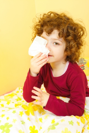 Little sick girl sitting in bed and blowing her nose.の写真素材