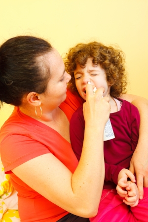 Caring mother clearing her daughter's nose with spray.の写真素材