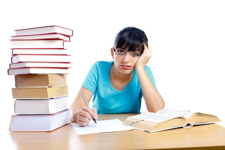 Bored and tired student girl looking to the camera and writing next to books on the table isolated on white - part of a series.の写真素材