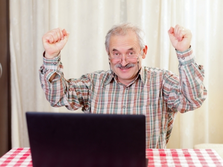 Elderly man with glasses using laptop at home.の写真素材