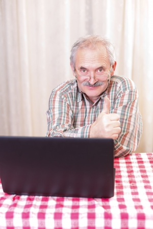 Elderly man with glasses using laptop at home.の写真素材
