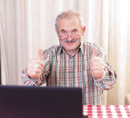 Elderly man with glasses using laptop at home.の写真素材
