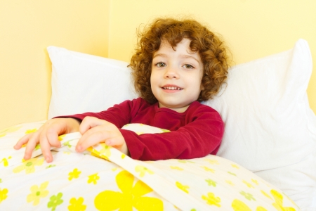 Curly haired girl laying in bed and smiling.の写真素材