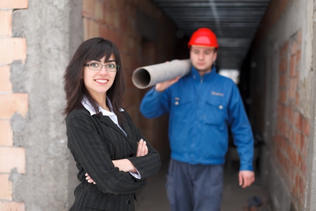 Happy businesswoman / employer smiling to the camera - a construction worker working in the background.の写真素材