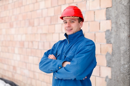 Confident construction worker smiling with folded arms next to brick wall.の写真素材
